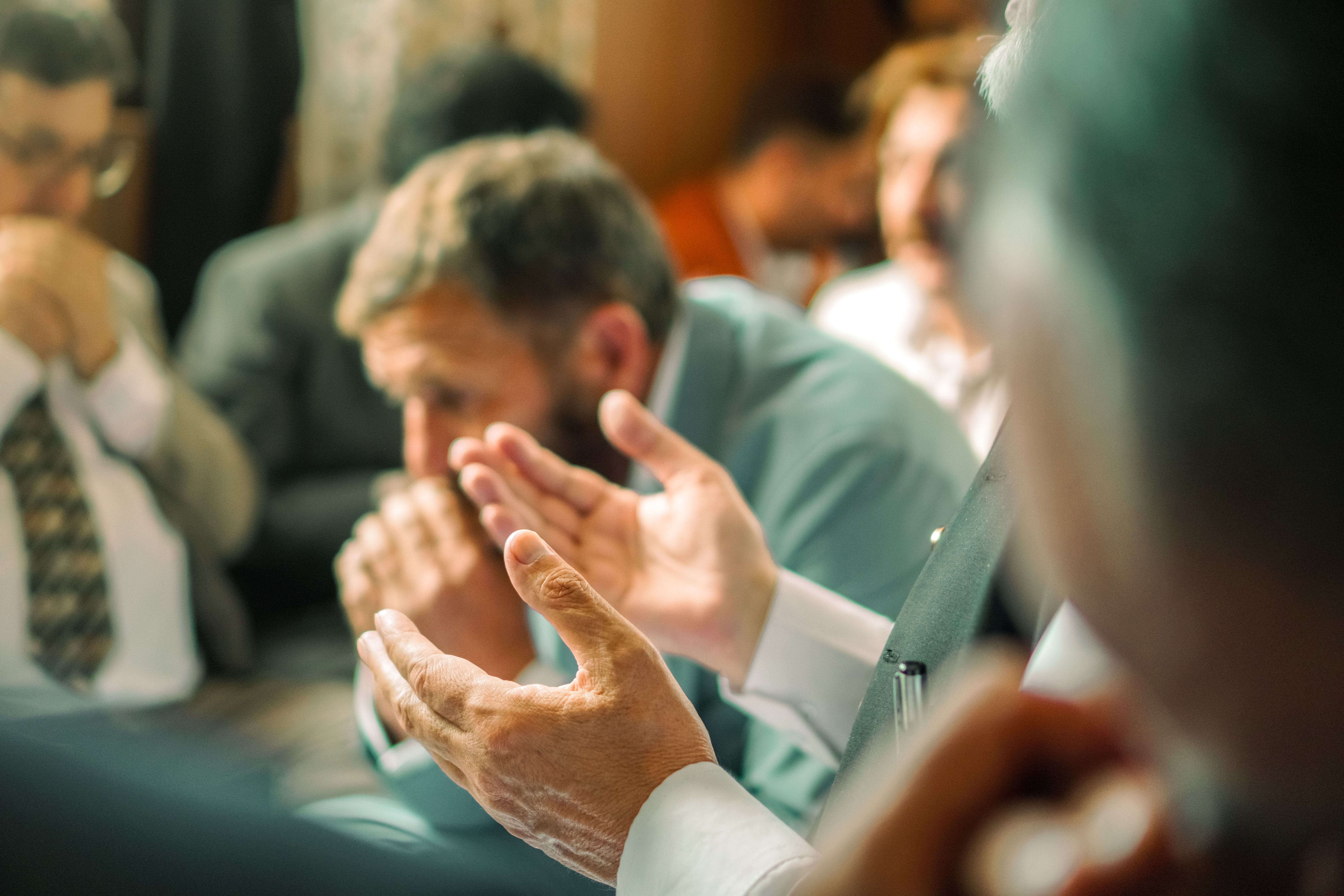 En réunion, une personne parle avec les mains tandis que les autres écoutent en silence.